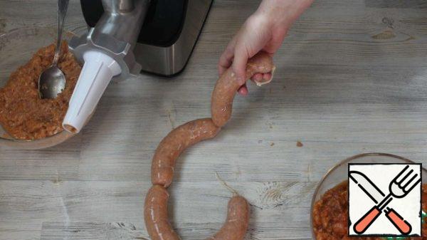 Now there are 2 ways.
Minced meat can be left in a bowl, covered with cling film and put in the refrigerator to marinate for a day. Then take out and stuff the sausages.
Or you can stuff sausages and leave them in the refrigerator overnight.
Stuffed seashells with stuffing.
Put the shell on the nozzle. Then squeeze out a little filling, remove excess air and tie the shell, form the beginning of the sausage. And then keep filling in. Stuffed sausages are prepared quite quickly and simply. When filling, make sure that the sausage is more or less uniform in thickness – without voids and dips. Very tight sausages are not stuffed with stuffing so that they do not burst when cooking. Then tie the end of the shell and twist it to make sausages of the desired length.
You can stuff it without a meat grinder: take a cut neck from a plastic bottle, where put the narrow part on the shell, and press the filling on the other side.
