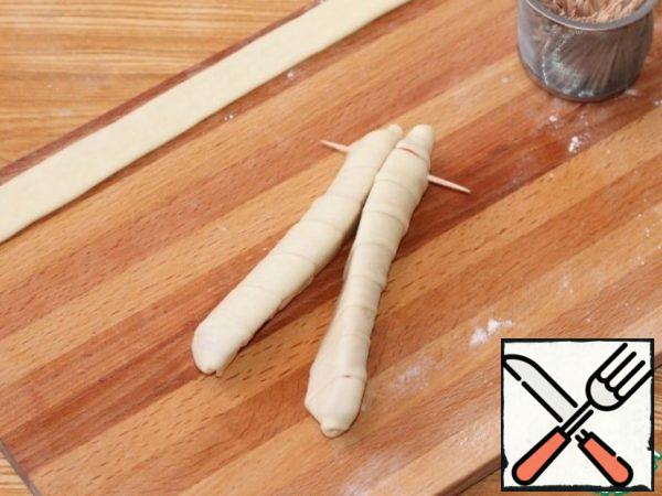 Take the sliced sausage and wrap each part (half) in a strip of dough.
