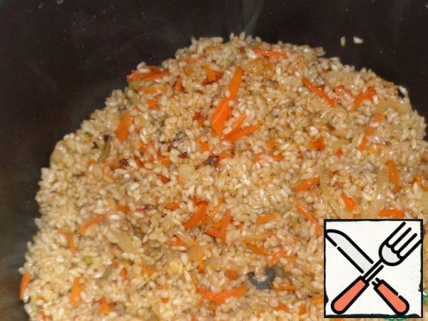 Rinse the rice until the water is transparent and put it in the bowl of a slow cooker with onions and carrots. Lightly fry it until golden brown. Do not close the lid!
