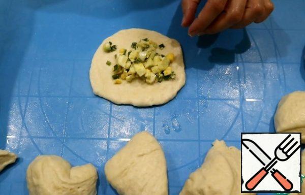 Put the finished dough on the table. Lubricate your hands and the surface with vegetable oil to make it easier to work with yeast dough.
Divide the dough into 32 parts. I divide the dough in half and each part into 16 parts.
Form a ball, roll out a round cake. Add 1-1.5 tablespoons of filling to the center and fix the edges well.
