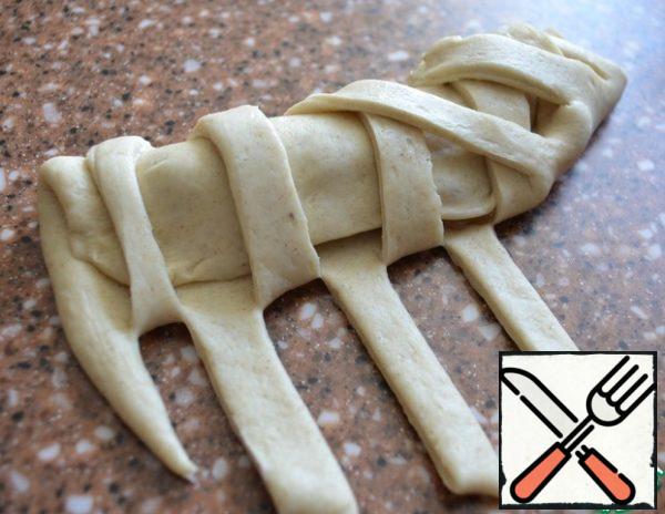 Fasten the strips, alternating them and at different angles.
Roll out the workpiece, giving the shape of a scallop.
Put it on a baking sheet.
