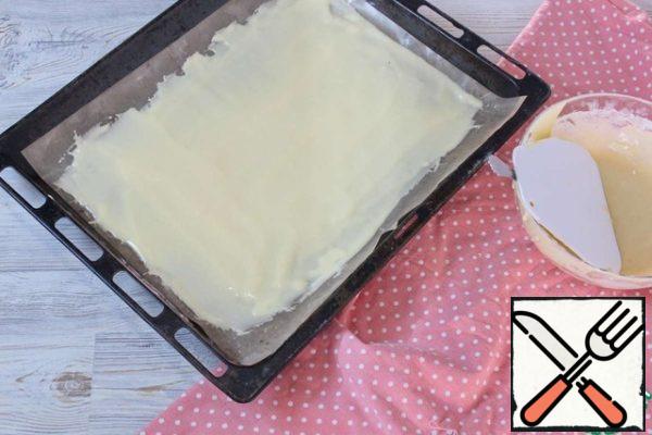 Start baking cakes.
You can bake round cakes, as in the classic recipe, but I'll make it easier.
We cover the baking sheet with parchment paper or a silicone mat, I have a baking sheet of 30 * 40 cm.
If you doubt the quality of the parchment, lubricate it with vegetable oil.
Divide the dough in half. Pour out 1 part of the dough and spread it in a small layer on a baking sheet. We try to distribute the dough as evenly as possible.
Put in a preheated 180 degree oven for about 7 minutes. As soon as the crust becomes golden, take it out.
Immediately cut off the uneven tips of the hot cake and cut into the required number of parts. Out of the total amount of dough, I got 8 cakes. Cut carefully, because the cakes are very tender.
Cool the cakes. Do not stack them on top of each other while they are hot, they may stick to each other.
Bake the second part of the dough in the same way.