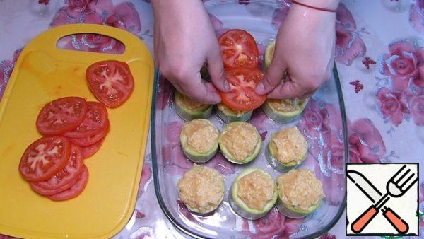 Cut tomatoes into thin slices according to the number of zucchini rings.
After 10 minutes, drain the water from the zucchini and put it in a greased baking dish.
Fill the zucchini rings with minced meat. Cover each stuffed zucchini with tomatoes.
