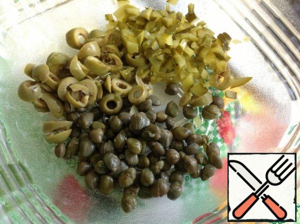 Put capers in a salad bowl, cut pickled cucumbers into small cubes, olives into slices.
