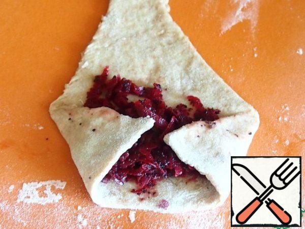 The edges of the wide side of the triangle slightly lengthen, shift towards the center and where they come into contact with the sides of the dough, press with your fingers.
