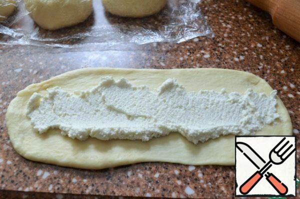 Roll out the smaller part into a circle, 8-10 cm..
Roll out coarsely into a long wide strip.
Put 2 tablespoons of cottage cheese filling on a strip.
