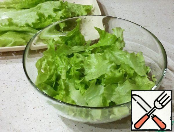 Wash the lettuce leaves and spread them on the bottom of a deep salad bowl.