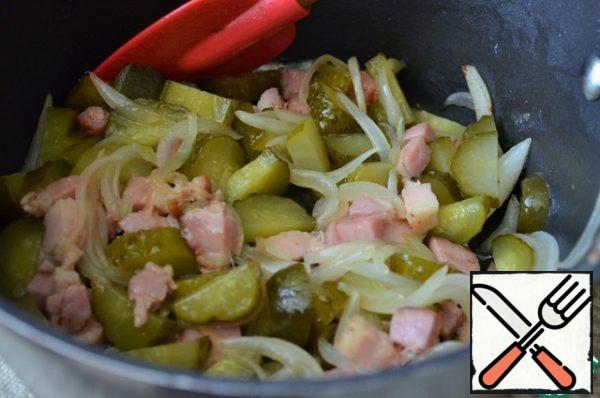 Add chopped feathers onion, fry until transparent.
Add slices of cucumbers and slices of sausage, fry for 5-7 minutes, stirring occasionally, over medium heat.