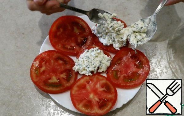 Tomatoes lay out on a plate and spread the cheese and garlic sauce. Serve immediately on the table.