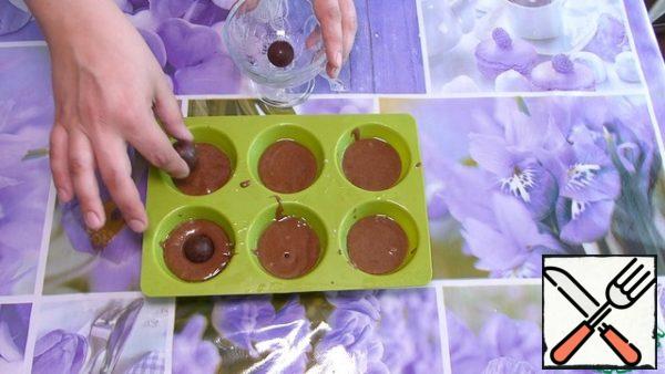 Silicone molds for baking grease with vegetable oil, fill 1 tbsp of dough.
Put 1 piece of candy.
Can be simply chocolate or raisins.