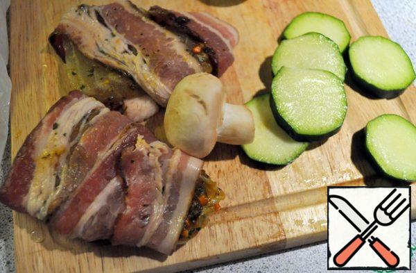 Fish cut into portions and each piece wrapped in a slice of bacon, cut zucchini (zucchini).