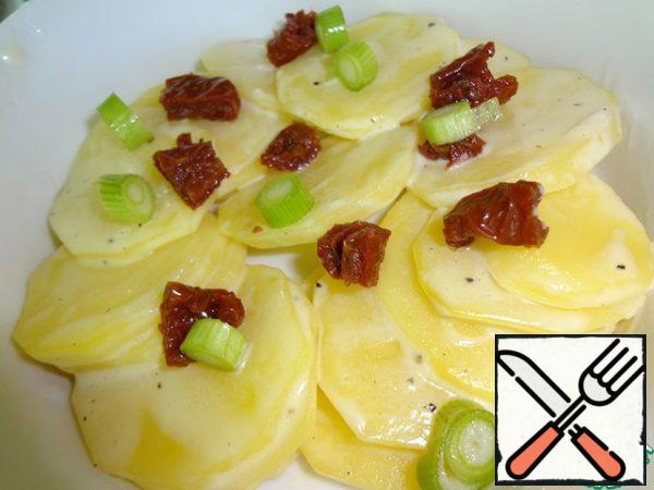 In a baking dish, put potatoes in a circle, green onions and dried tomatoes on it.