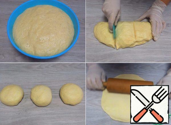 I put the dough to rise in a warm place for at least an hour, and preferably for an hour and a half. Transfer the dough that has come up to the work surface, divide into 3 equal parts, give a rounded shape. We roll out each bun into a circle with a diameter of about 25 cm .
