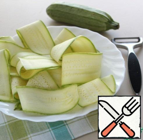 With a vegetable peeler or grater to cut thin ribbons of zucchini.
