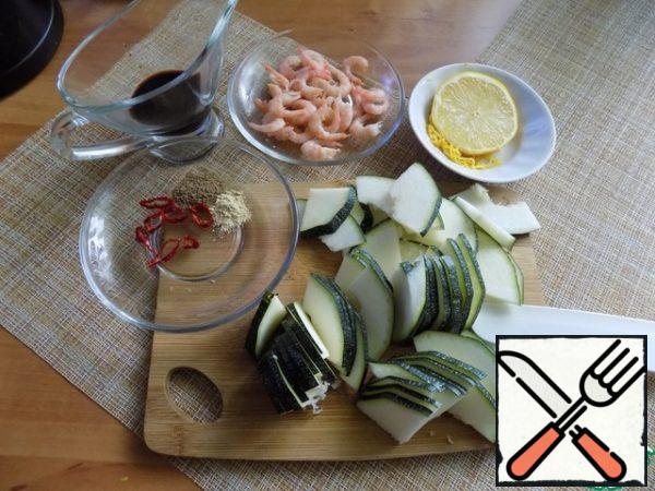 My prawns are already boiled and frozen. Defrost and clean. Products need to be prepared all at once. Remove the zest from the lemon, cut a slice of lemon to get juice. Cut the zucchini into thin slices. It's big, and I cut it into thin slices. From the chili pepper, cut off several rings, removing the cores.

