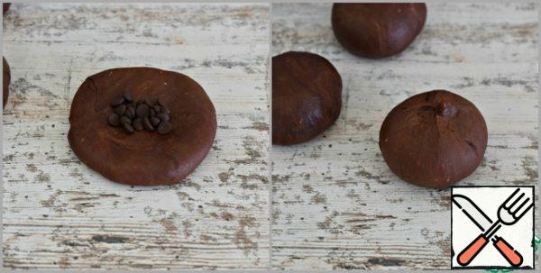 Roll out each blank into a flat cake, put 10-13 chocolate drops or an incomplete teaspoon of dark chocolate grated on a coarse grater in the middle of the cake.
Lubricate the edges of the cake, forming a round bun.
