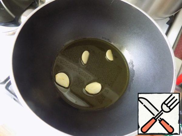 Fry vegetables in parallel with a frying pan or saucepan. I poured oil into a saucepan, warmed it up and put garlic cloves, cut lengthwise into 2 parts. Fry the cloves for a minute so that they give their flavor to the oil. They can be thrown away. I left them, I'll put them away later.

