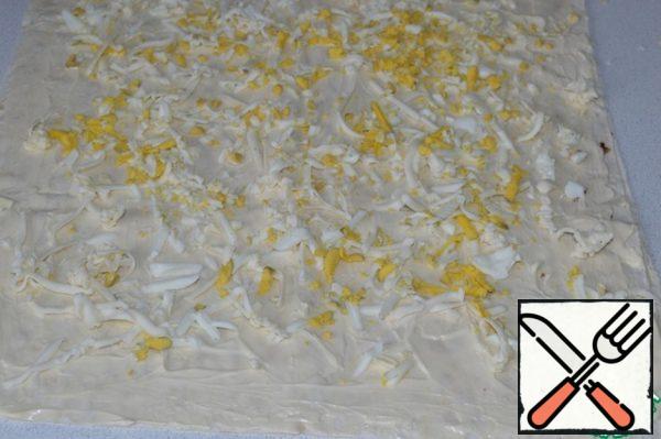 Smear a sheet of lavash with mayonnaise, cover with a second sheet of lavash and also smear with mayonnaise.
Grate the melted cheese and eggs on a coarse grater and spread over the entire surface of the pita bread.
