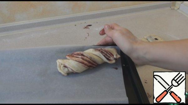 Take the cut strip and twist it with a flagellum. Spread on a baking sheet covered with parchment paper. Similarly, twist all the buns. Leave the buns for 5 minutes, so that they come up a little.