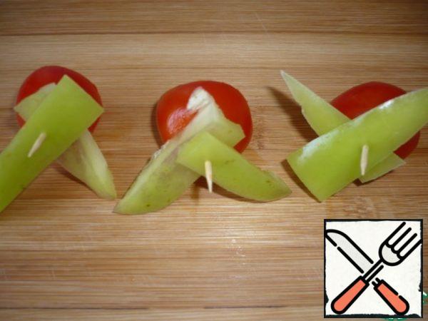 On a toothpick, string slices of green bell pepper crosswise and half a cherry tomato.
