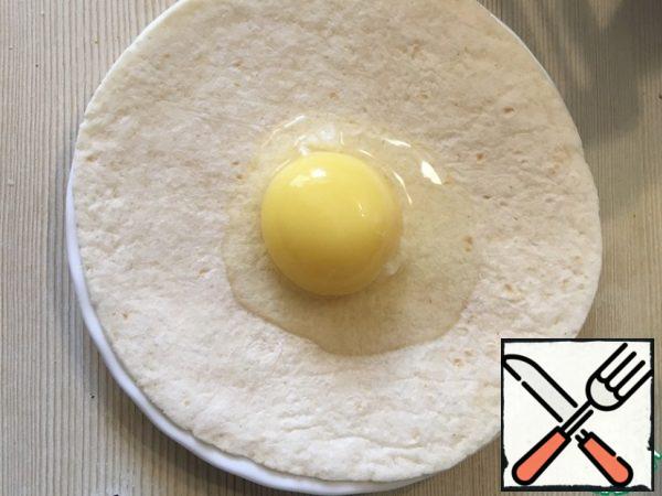 Put the tortilla on a plate with a shallow bottom, pour half an egg there.