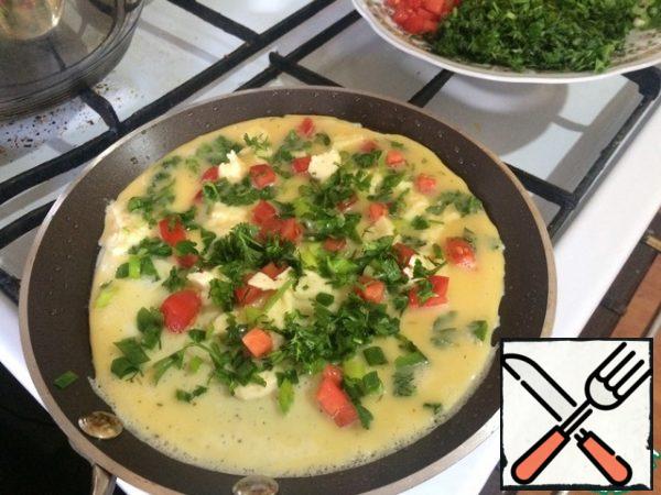 On a slightly heated frying pan, already greased with vegetable oil, pour part of our egg-milk mixture, as if we want to fry a pancake. I recommend taking a non-stick frying pan to make it easy to cook. Pour a little cheese, herbs, onions and tomatoes on the "pancake". Cook over low heat.
