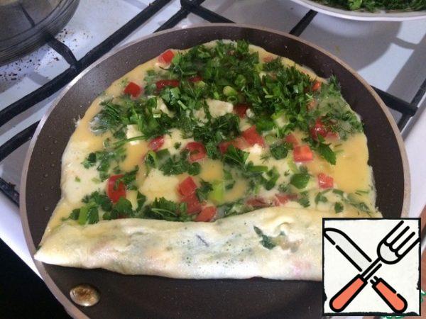 On the part of the pancake added to the pan, pour again the cheese, herbs, onions and tomatoes.