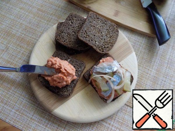 I'm going to do small plates for toast of Borodino bread. Bread can take any and just spread on top of this spread. It's delicious and heartfelt. I spread generously each piece of Borodino bread, put on top of herring fillets and pickles, cut arbitrarily. She spread thin half-rings of pickled onions on top. Onions are delicious.