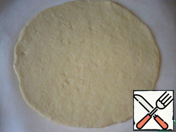 Then transfer the dough to the baking parchment ( because on the parchment it will be more convenient to transfer the cake to the baking sheet) and roll out into a layer in the form of a circle.