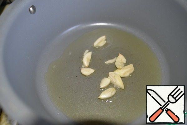Garlic peel, crush with a knife. Take a saucepan or pan with a thick bottom, heat the oil, put the garlic.