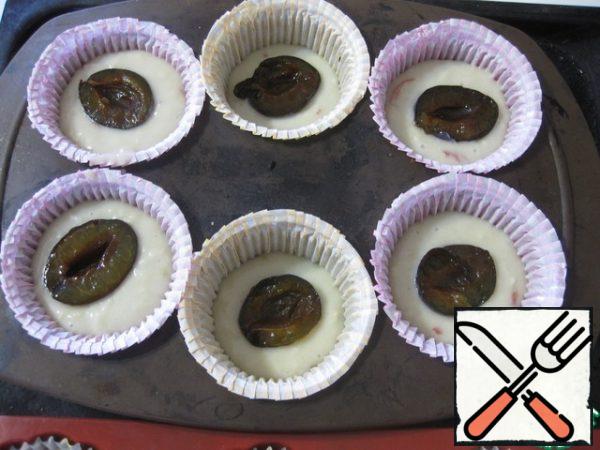 Prepare molds for muffins, - I have silicone, they are lined with paper cuffs, - and put the dough on 2/3. On the dough put half of the plums, cut up (plum prepare in advance). In medium molds plums laid out in the middle of the dough,