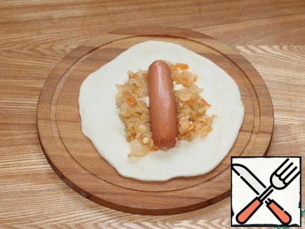 Roll out each part of the dough into a flat cake. Put 2 tablespoons of cabbage and half a sausage on each tortilla.
