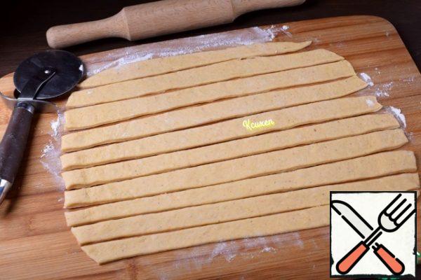 Using a small amount of flour, roll out the dough with a rolling pin into a thin layer and cut it into strips 2-3 cm wide.