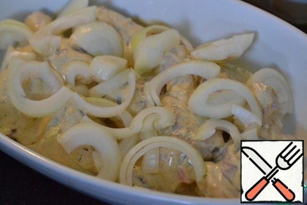 A bowl for baking grease with sunflower oil.
Lay out the chicken drumsticks.
From above add sliced half rings onion.