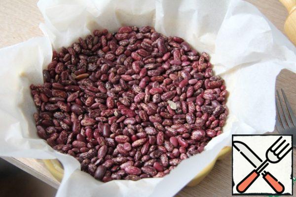 Cover the dough with parchment and pour in a "weighting agent" (peas, beans or special bones).
Bake with this load at a temperature of 200 degrees for about 10-12 minutes. Remove the paper along with the load.
