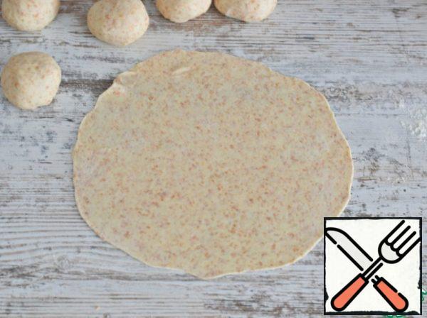 Lightly sprinkle the work surface with flour. (In total, 10 grams will be enough for one serving)
From each billet, roll out a thin cake with a diameter of 20 cm. the diameter of the cake should be equal to the diameter of the frying pan on which you will fry the cakes.
The dough turns out to be very obedient and pliable, and it will not be difficult to roll out a cake with a thickness of one and a half to two mm.
