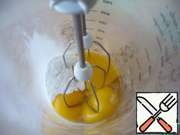 While the first layer is baked, prepare the second. Grate the zest of one lemon, and squeeze the lemon juice. We will need 1 tbsp. Beat the egg yolks with powdered sugar. The mass should increase in volume.