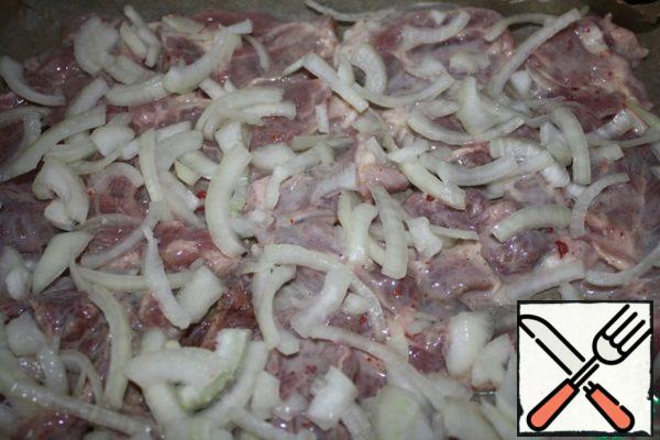 At the bottom of the pan with high sides put in a single layer of meat without marinade. Cut the onion into half rings and meat.