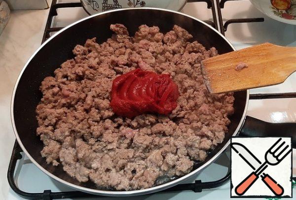 Spread the minced meat on a preheated and greased with vegetable oil pan. After the minced meat is stewed for 5-7 minutes, add salt and tomato paste.