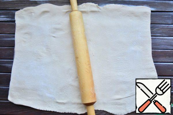 Roll out puff pastry. It is better to do it immediately on parchment paper. So it will be easier to form a strudel and transfer it to the oven.
To ensure that the dough does not stick to the parchment, use starch.