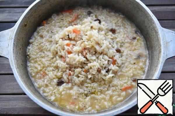 Next, cover the rice with raisins, gently pour in cold water and bring to a boil over high heat. When the water level reaches the rice level, collect the slide from the edges to the center, reduce the heat to a minimum. Put a deep plate of the appropriate diameter on top of the rice, cover it, then with a clean kitchen towel and cover the whole structure with a lid.

