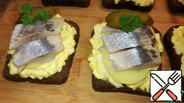 Next to the pickle, spread the herring cut into thin pieces in two pieces. And garnish with parsley.