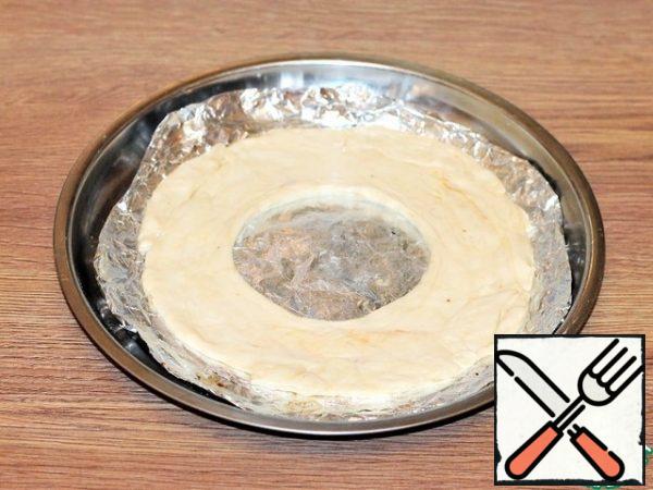 Cover the mold (f=26 cm) with foil or baking paper and use a rolling pin to transfer the circle of dough. Cut a circle in the middle, equal to the diameter of the glass. Grease the circle with melted butter and pierce with a fork.
