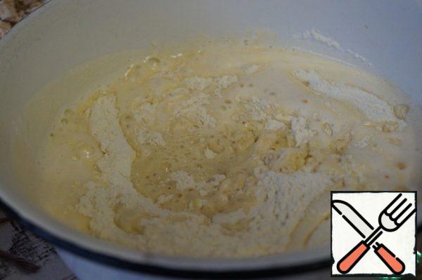 In the flour, make a recess, pour in the olive oil, pour the milk with yeast and beaten eggs.