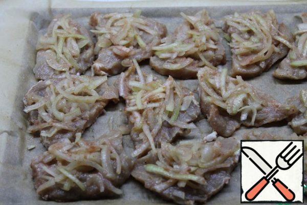 On a baking sheet covered with parchment, put the pieces of meat, and on top of them distribute the onions from the marinade. Bake in a preheated 200 degree oven for 30 minutes. You can cover the top with foil. While the meat is cooking, cut the garlic into thin slices and grate the cheese. Get the meat, distribute the chopped garlic and sprinkle with cheese, send in the oven for another 10 minutes.