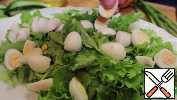 In a dish for cooking, put the lettuce leaves, after separating the thick stems, and the leaf-tear with your hands to an average size. Boil and peel the quail eggs, divide them in half, put on top of the salad leaves.