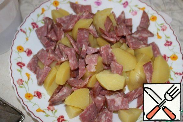 Cut the sausage into thick strips. Spread on a dish with potatoes.