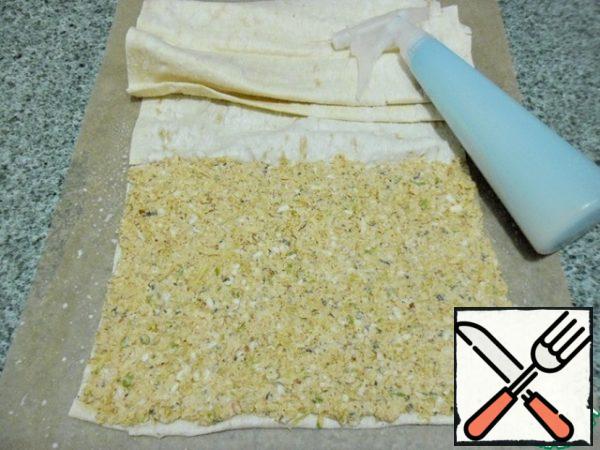 Spread a sheet of baking paper on the table, and on it pita bread, which you mentally divide into 4 parts.
Part 1-zucchini filling
Part 2 - the first part scrolls a few turns just in the pita bread.
Part 3-the second filling with tomatoes and pepper
Part 4 is just pita bread again.
Milk can be applied to pita bread with a brush, but I poured it into a spray bottle (I have it for cooking, don't think about what).
Sprinkle lavash liberally, now it will not clump and tear.
Lay out the zucchini filling in an even layer.
See the photo
