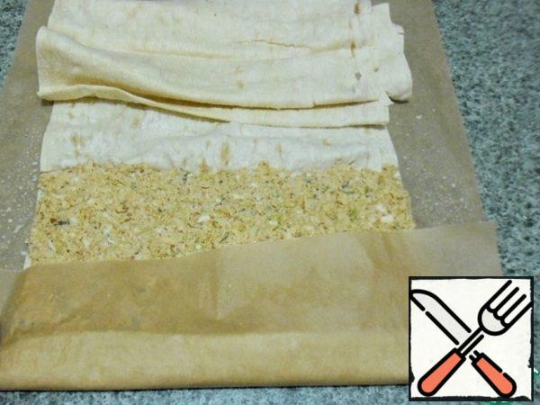 With the help of parchment wrap the edge, tightly press down and twist the roll.