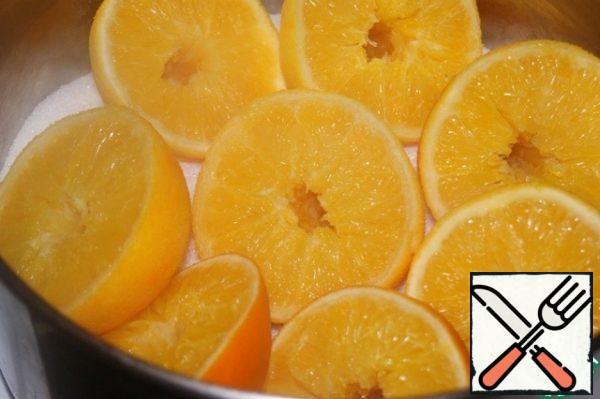 In a saucepan, pour half the sugar and place the oranges on it.